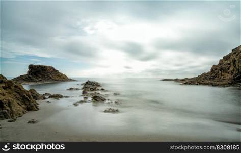 A long exposure of a picturesque small beach in a rocky cove with reef at low tide