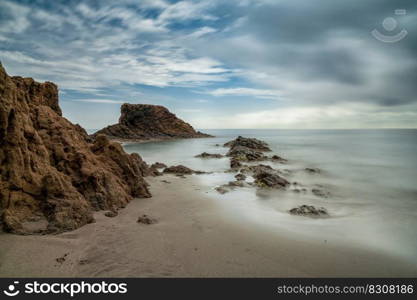 A long exposure of a picturesque small beach in a rocky cove with reef at low tide