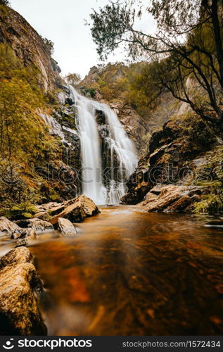 A long exposure shot of a massive waterfall in the middle of the forest during autumn