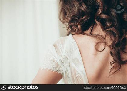 A long haired brunette bride in unbuttoned white dress, a closeup view from the back