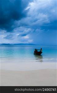 A long-tail boat moored while waiting for tourists on an island beach during monsoon, a dark rainstorm covers the Andaman Sea in the background. South Thailand. Environment, tourism concepts.