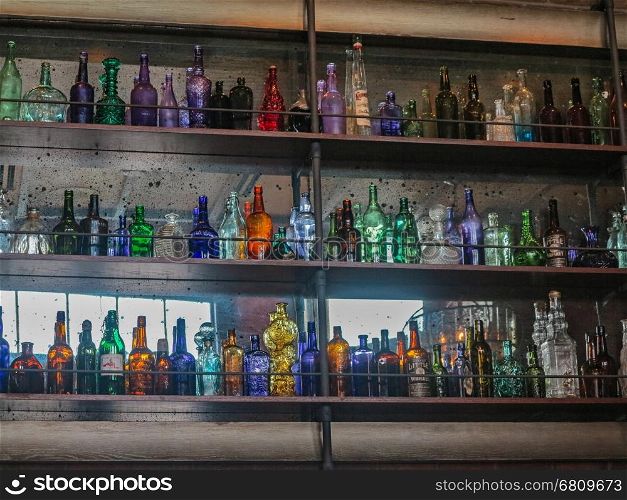 A lot of different colored glass bottles on shelves.