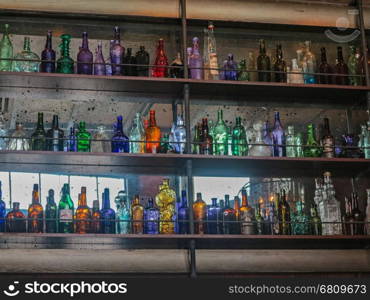 A lot of different colored glass bottles on shelves.