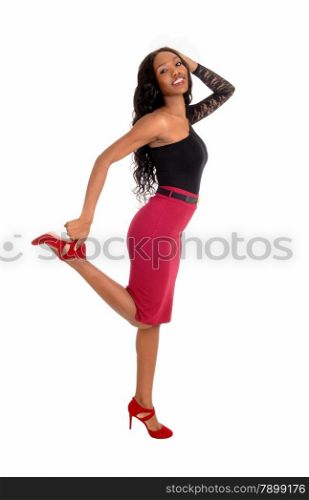 A lovely African American woman in a red skirt and black blouse holdingher leg up, smiling, isolated for white background.