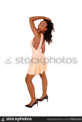A lovely African Amerikan woman in a beige dress with long curly blackhair, looking over her shoulder, isolated for white background.