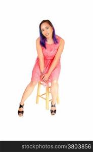 A lovely Asian woman sitting on a chair in a nice pink dress, looking intothe camera, isolated over white background.