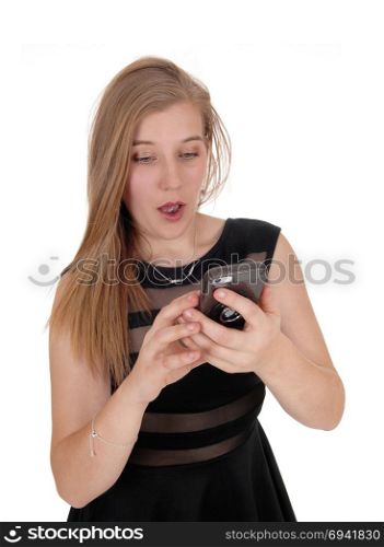 A lovely blond woman in a black dress looking in disbelief at her cellphone is disgusted about the message, isolated for white background