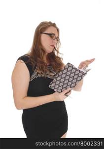 A lovely blond woman standing waist up in a black dress and glasses,reading in her journal, isolated for white background.