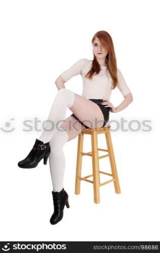 A lovely brunette woman sitting on chair in shorts and long white socksand high heels with legs crossed, isolated for white background