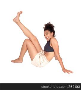 A lovely multi-racial woman in a black top and beige shorts sitting in the studio on the floor with her curly black hair in a bun and lifting one leg, bare foot, isolated for white background