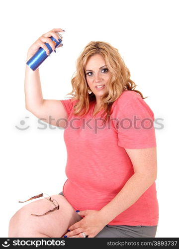 A lovely plus size woman sitting in shorts on a chair and spraying hairspray on her hair, isolated foe white background.