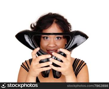 A lovely young mixed raced woman holding her black high heels onher face, looking trough, isolated for white background.