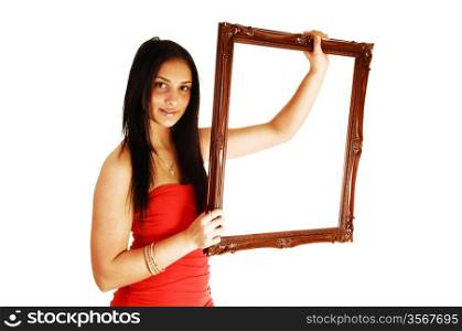 A lovely young teen girl in a red dress, holding up a picture frame with herlong black hair standing in the studio for white background.