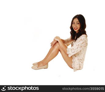 A lovely young woman in a beige short dress sitting on the floorwith her long brunette hair, for white background.