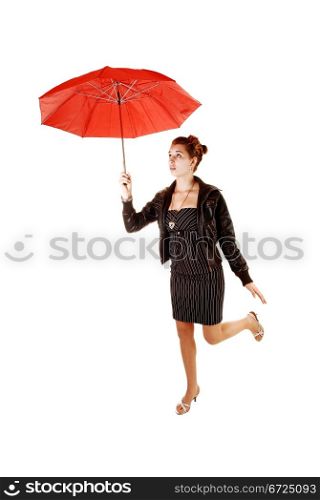 A lovely young woman in a black dress and brown leather jacket and highheels standing on one leg for white background holding up a red umbrella.