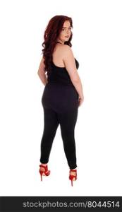 A lovely young woman in a black jumpsuit and red high heels standingfrom the back, looking over her shoulder, isolate for white background.