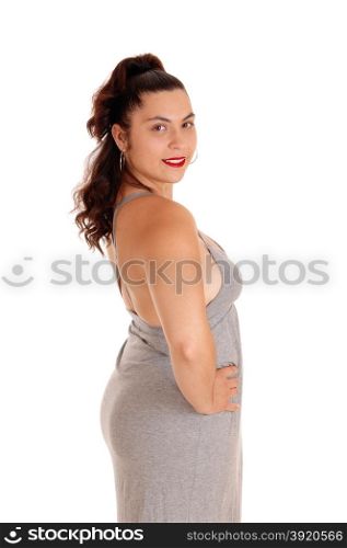 A lovely young woman standing in profile in a gray dress, isolatedfor white background, looking into the camera.