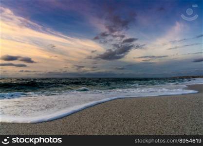 A low angle view of white sand beach with waves rolling in under a colorful sunset sky