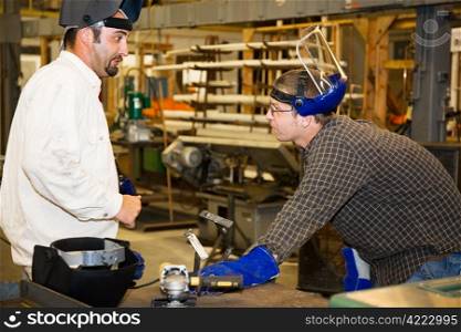 A machinist in a factory listens as his supervisor critiques metal working project. Authentic and accurate content depiction in accordance with industry code and safety regulations.
