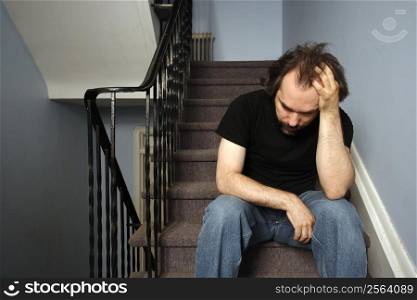 A male adult with serious depression sitting in the stairwell of his apartment building.