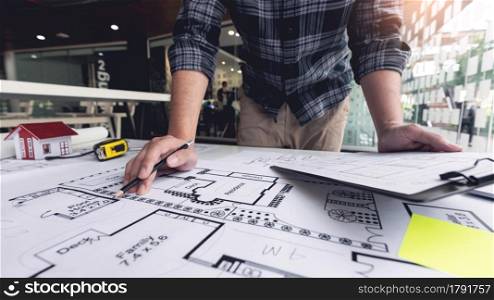 A male architect measuring and marking the scale ratio of sizes of a complicated blueprint.