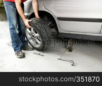 A male changing a tire on a car in a garage