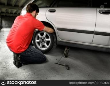 A male chaning a tire on a car in a garage
