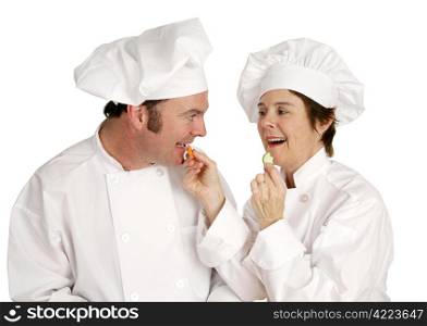 A male chef eating a carrot fed to him by his female colleage. Focus on the male.