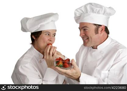 A male chef feeding a fresh strawberry to a female chef. Isolated on white.