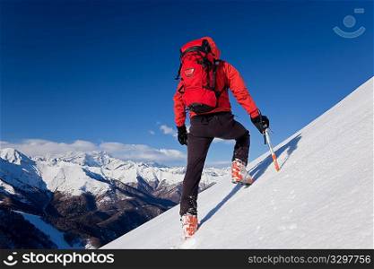 A male climber , dressed in red, climbs down a snowy slope. Winter clear sky day. In background the Monte Rosa massif, Italy, Europe.