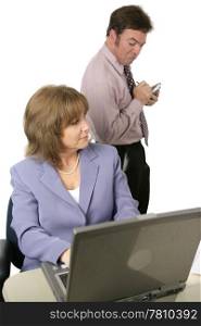 A male coworker spying over a female coworker&rsquo;s shoulder and taking notes on what he sees. Isolated on white. Focus on female.
