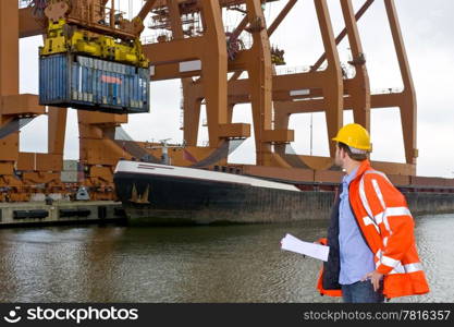 A male customs control officer inspecting the unloading of containers at an industrial harbor