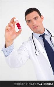 A male doctor examining a blood sample, the focus is on the vial of blood.