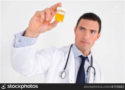 A male doctor examining a urine sample. The focus is on the sample bottle.