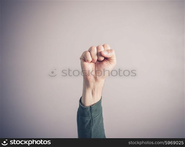 A male fist is clenched and raised in the air against a light purple background