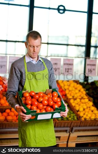 A male grocery owner with a box of ripe tomatoes