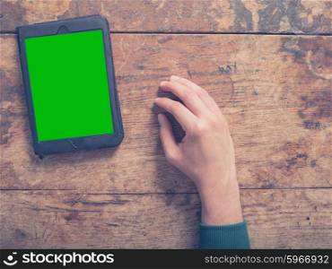 A male hand and a tablet computer with a green screen on a wooden table