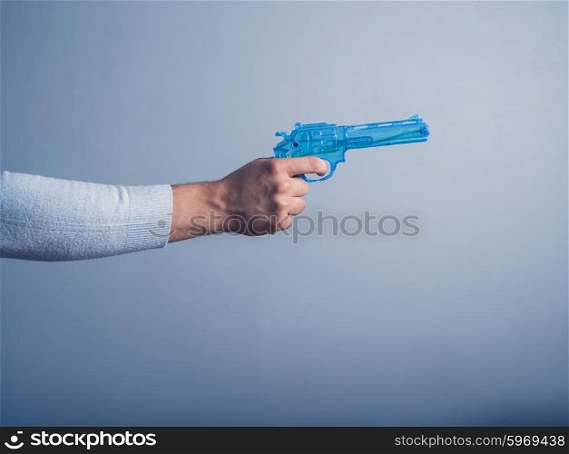 A male hand is holding a blue water pistol and is aiming it