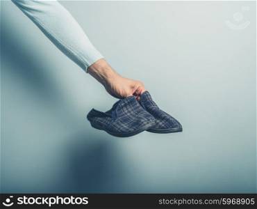 A male hand is holding a pair of slippers