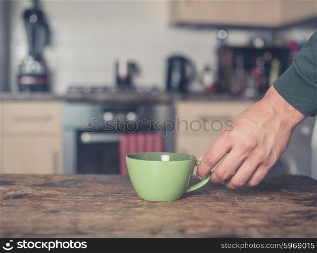 A male hand is placing a cup on a table in a kitchen