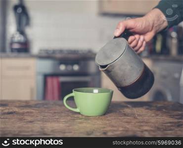 A male hand is pouring coffee into a cup in a kitchen from a moka espresso pot