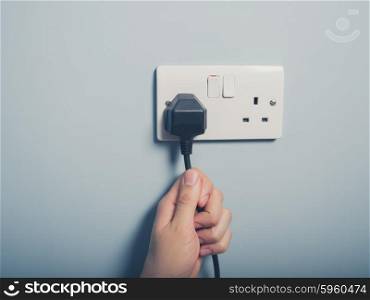 A male hand is pulling an electrical cord plugged into a wall socket