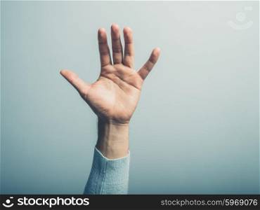 A male hand is waving in front of a blue wall