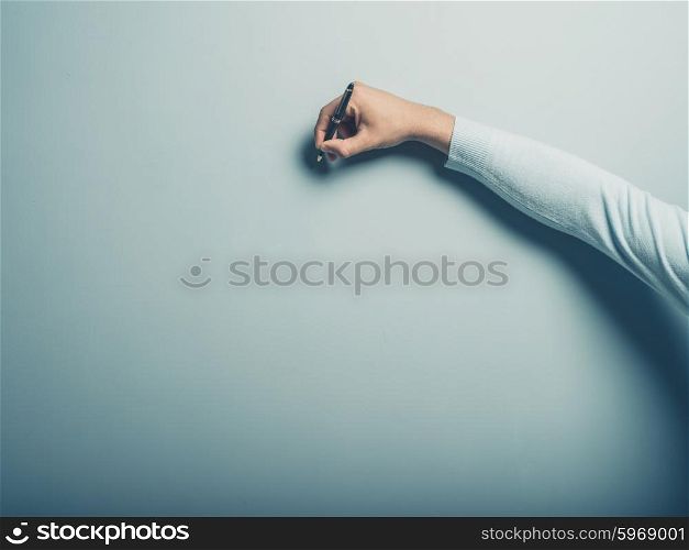 A male hand is writing on a blue wall with a pen