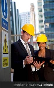 A male manager on a construction site wearing a hard hat and talking with his Asian female colleague