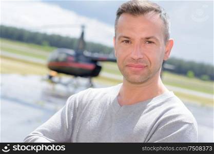 a male mechanic posing with an helicopter in the background