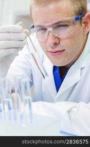 A male medical or scientific researcher or doctor looking at a test tube of clear liquid in a laboratory with microscopes.