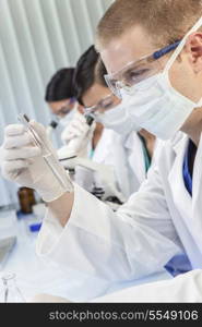A male medical or scientific researcher or doctor looking at a test tube of clear liquid in a laboratory with female colleagues.