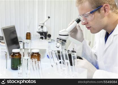 A male medical or scientific researcher or doctor using a microscope in a laboratory with test tubes.