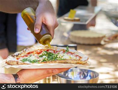A male pouring olive oil to season a pizza. Italian cuisine. traditional Italian recipe.